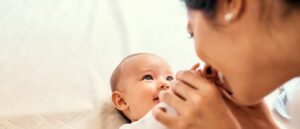 A baby laying down on back with a woman holding the baby's hands, kissing them.