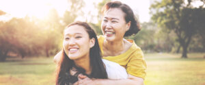 Two women smiling, one older, hugging a younger woman over the shoulders.