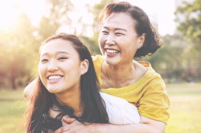 Two women smiling, one older, hugging a younger woman over the shoulders.